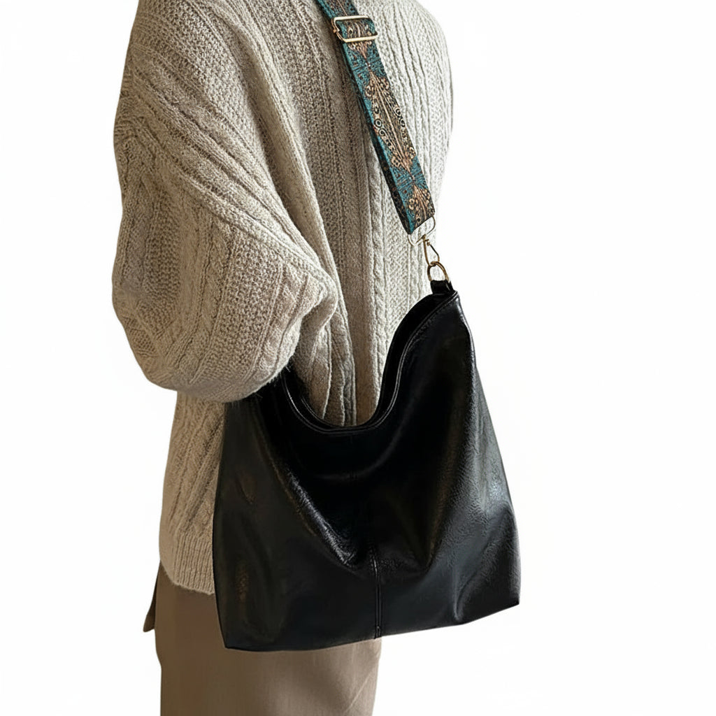 Black handbag hanging on a mannequin with a beige sweater in a room setting.