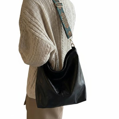 Black handbag hanging on a mannequin with a beige sweater in a room setting.