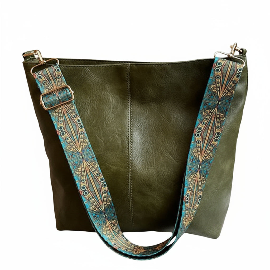 Green leather handbag with decorative strap on a surface near a window.