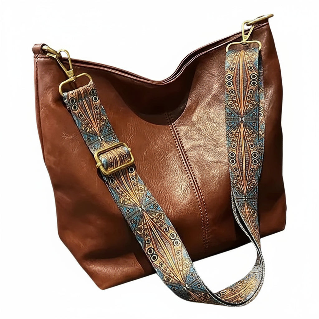 Brown leather handbag with a decorative strap on a neutral background