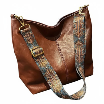 Brown leather handbag with a decorative strap on a neutral background