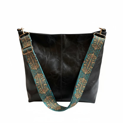 Black leather handbag with decorative blue and gold strap on a surface.