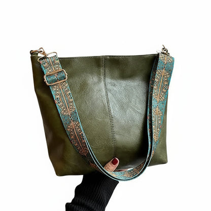 Green handbag with decorative strap held by a person in front of a window.
