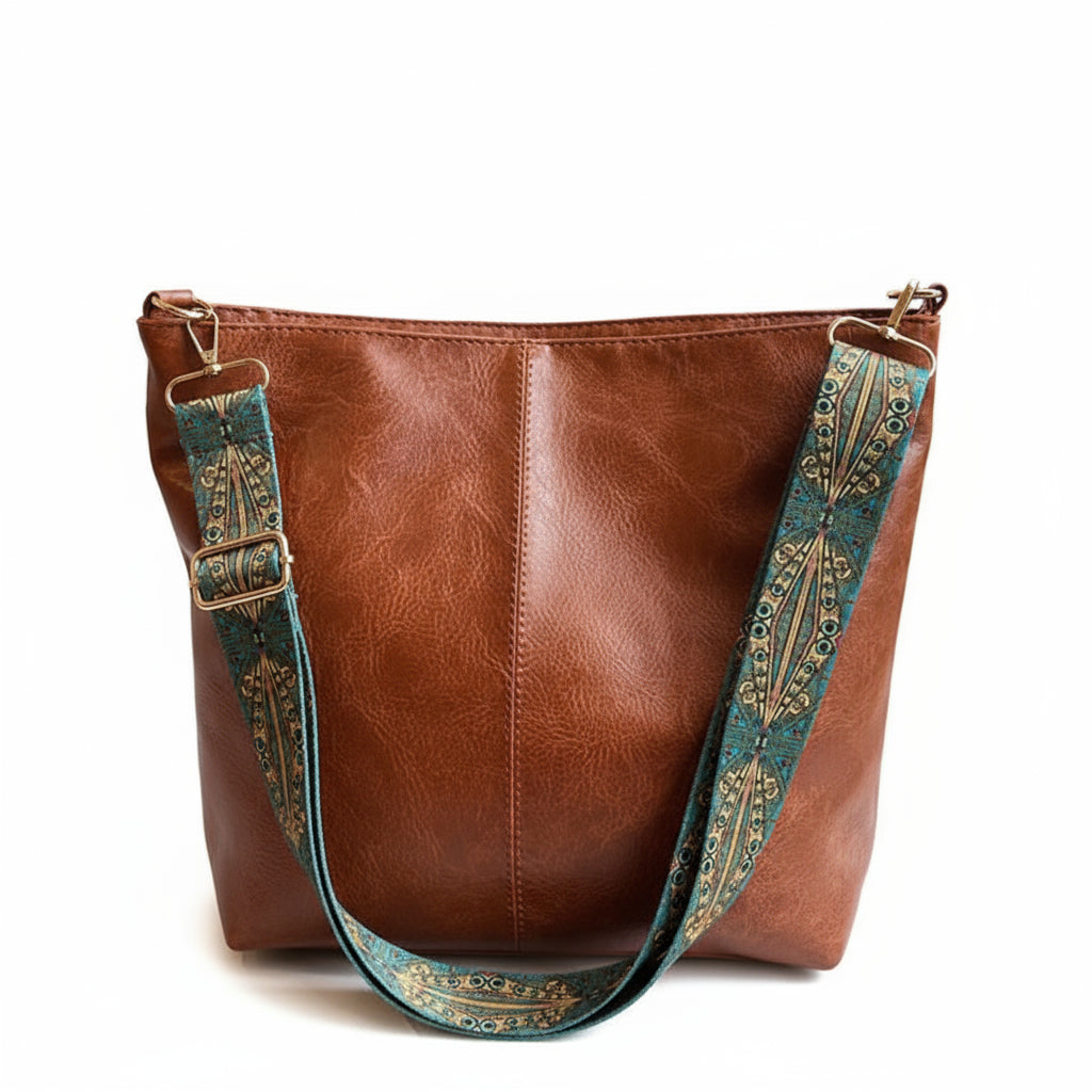 Brown leather handbag with a decorative blue strap on a surface near a window.